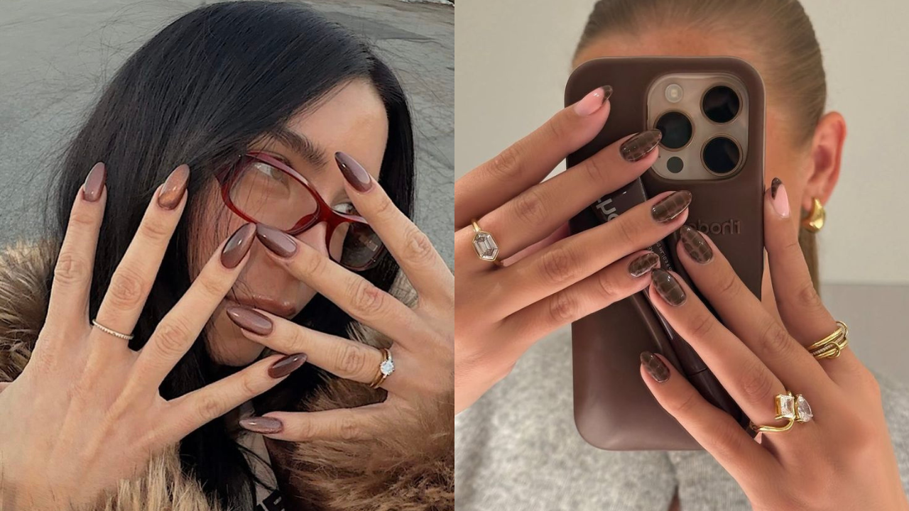 Duas mulheres exibem unhas longas e escuras em tons de marrom. A da esquerda usa óculos vermelhos e anéis finos, enquanto a da direita segura um celular marrom e exibe anéis com pedras