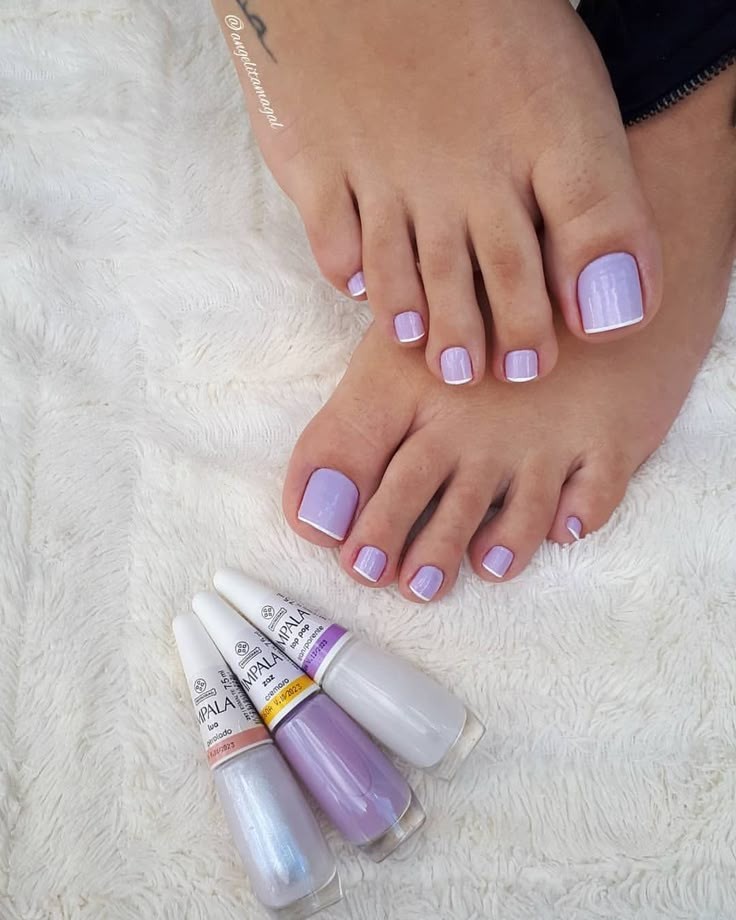 P&eacute;s femininos com unhas pintadas de lil&aacute;s e francesinha branca, sobre um tapete branco felpudo. Tr&ecirc;s esmaltes Impala, um perolado, um lil&aacute;s cremoso e um branco, est&atilde;o ao lado dos p&eacute;s