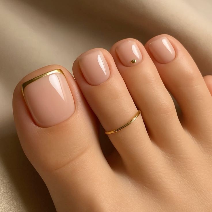 P&eacute;s com unhas pintadas de rosa claro e acabamento brilhante. O ded&atilde;o tem uma linha dourada na base da unha, e o dedo m&eacute;dio tem um pequeno ponto dourado. Um anel fino dourado adorna o dedo anelar