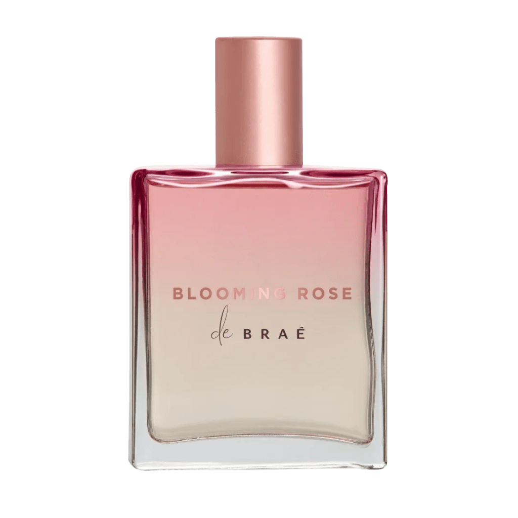 Frasco de perfume quadrado com l&iacute;quido em degrad&ecirc; rosa claro para bege, tampa e letras BLOOMING ROSE em cobre met&aacute;lico, e de BRA&Eacute; em preto