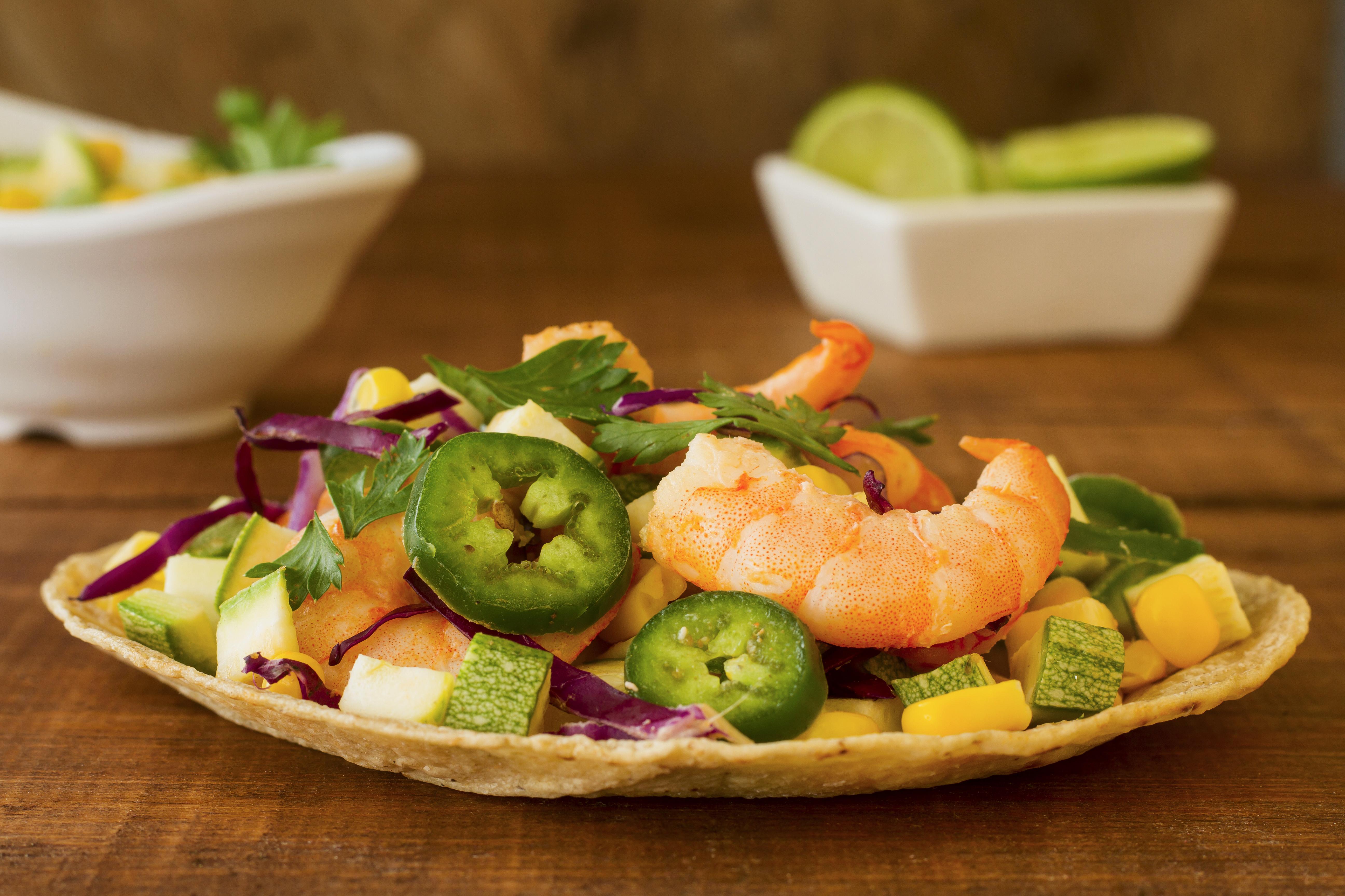 Tostada mexicana com camar&otilde;es, milho, abacate, repolho roxo, piment&otilde;es jalape&ntilde;o e coentro fresco sobre uma mesa de madeira r&uacute;stica