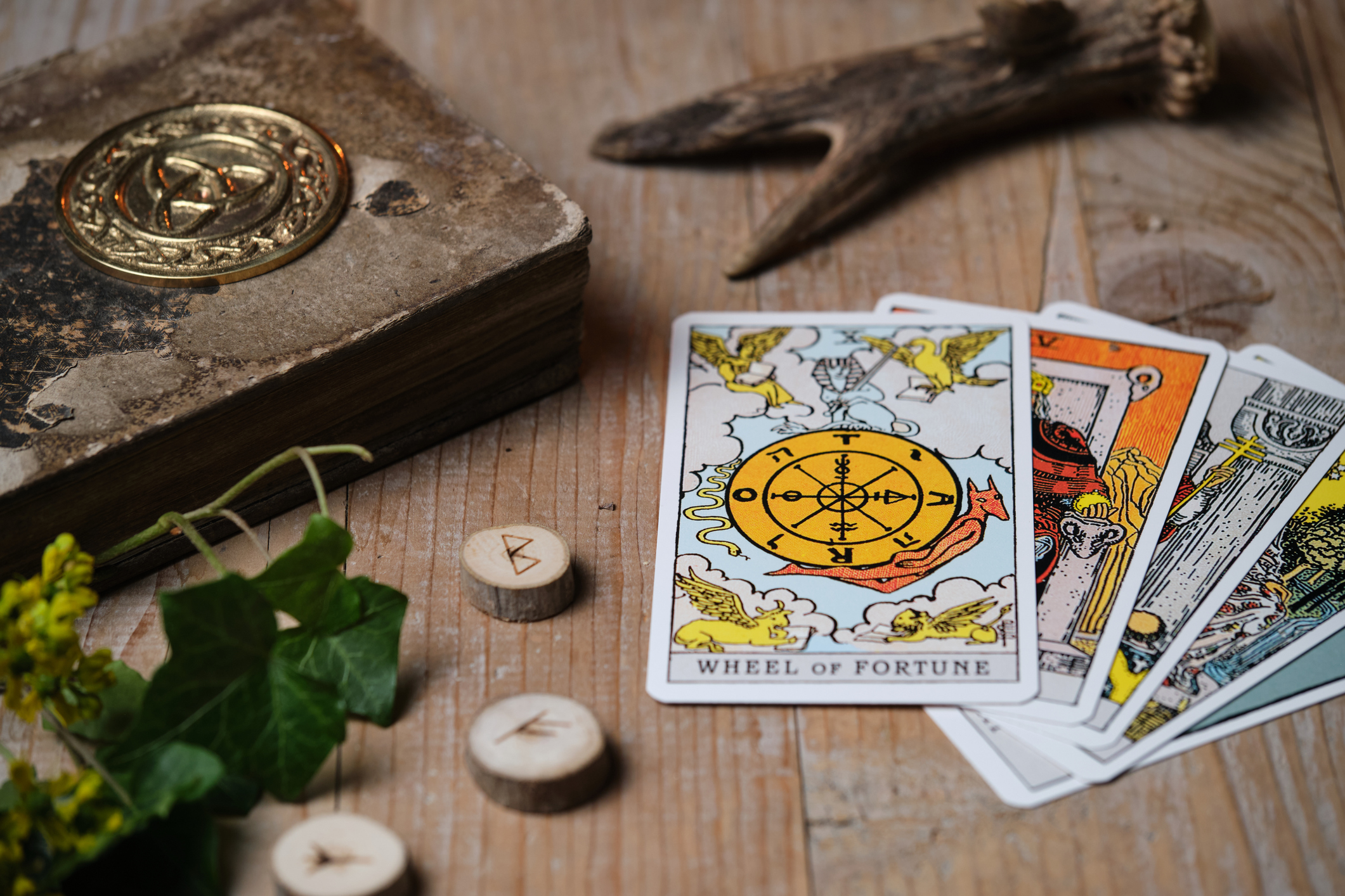 Tarot cards and runes on an old wooden table, “Wheel of Fortune” card placed on top – moody mystic scene