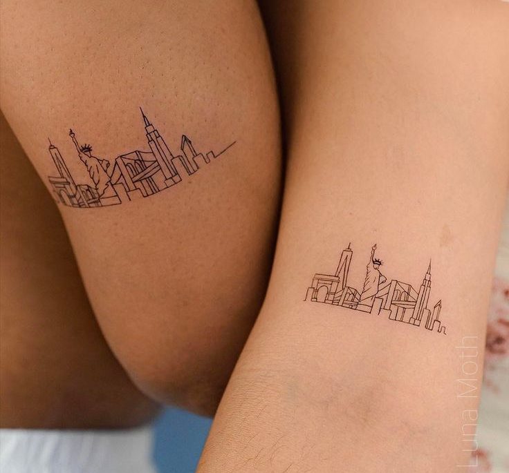 Duas pessoas com tatuagens de contorno da silhueta de Nova York, incluindo a Est&aacute;tua da Liberdade e arranha-c&eacute;us, uma na coxa e outra no antebra&ccedil;o