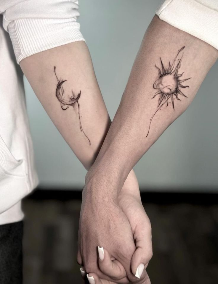 Dois antebra&ccedil;os se cruzam, com as m&atilde;os dadas na parte inferior. O bra&ccedil;o esquerdo tem uma tatuagem de lua crescente, e o direito, uma de sol, ambas em estilo aquarela com tra&ccedil;os finos e pretos