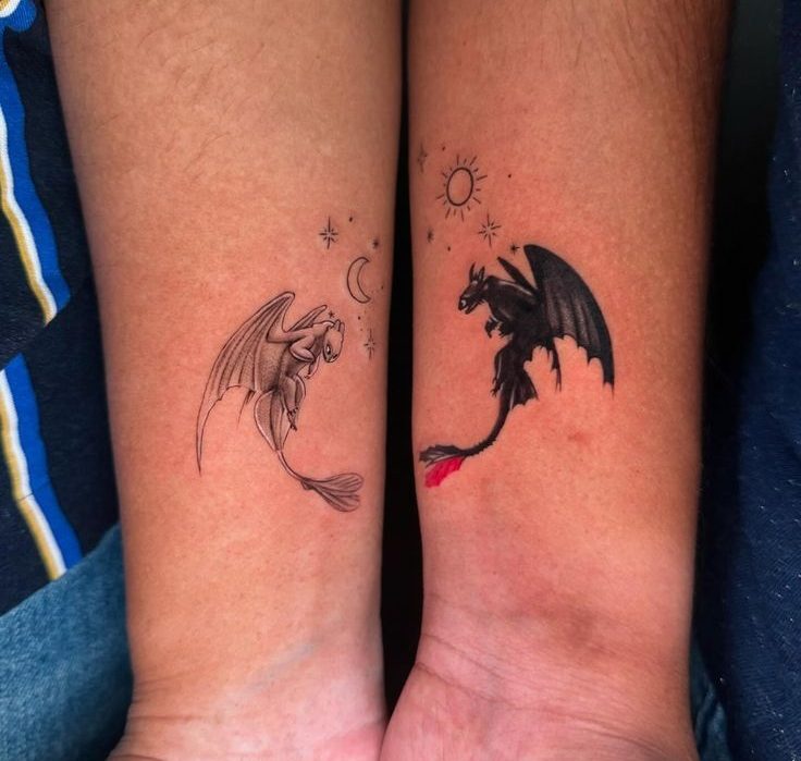 Dois antebra&ccedil;os lado a lado exibem tatuagens de drag&otilde;es. No esquerdo, um drag&atilde;o branco com asas abertas e uma lua crescente. No direito, um drag&atilde;o preto com asas abertas, cauda vermelha e um sol.