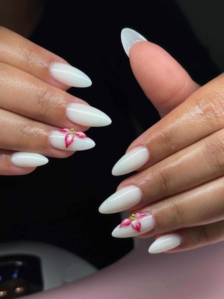 M&atilde;os com unhas amendoadas brancas, uma flor rosa com miolo dourado pintada no anelar de cada m&atilde;o, fundo escuro