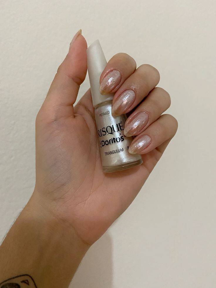 M&atilde;o feminina segurando um esmalte Risqu&eacute; & Doritos met&aacute;lico, com unhas pintadas na mesma cor cintilante e alongadas