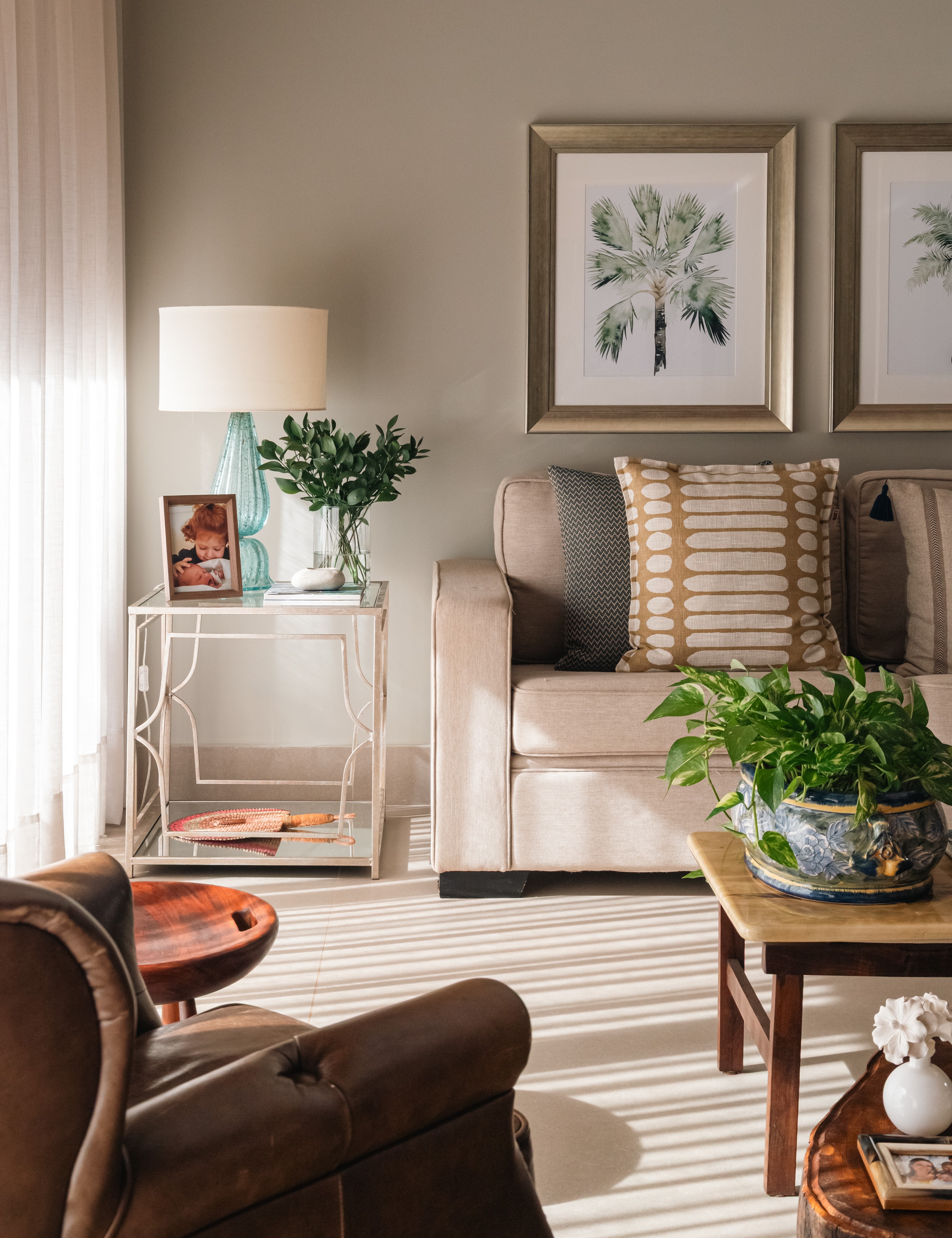 Sala de estar elegante e acolhedora, com tons neutros, m&oacute;veis de madeira e couro, plantas e detalhes naturais. Na mesa lateral, o porta-retrato acrescenta um toque pessoal e afetivo &agrave; decora&ccedil;&atilde;o. A ilumina&ccedil;&atilde;o suave valoriza a composi&ccedil;&atilde;o e cria uma atmosfera leve e sofisticada.