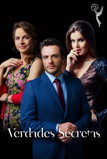 Tr&ecirc;s pessoas em fundo preto: um homem de terno azul e gravata vermelha no centro, uma mulher de vestido floral &agrave; esquerda e outra de vestido brilhante &agrave; direita, com a m&atilde;o na boca. No canto superior direito, o logo do Emmy. Na parte inferior, o t&iacute;tulo Verdades Secretas