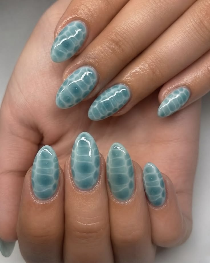 M&atilde;os com unhas ovais longas, esmalte azul-turquesa com efeito 3D de bolhas ou escamas, lembrando &aacute;gua ou pele de r&eacute;ptil