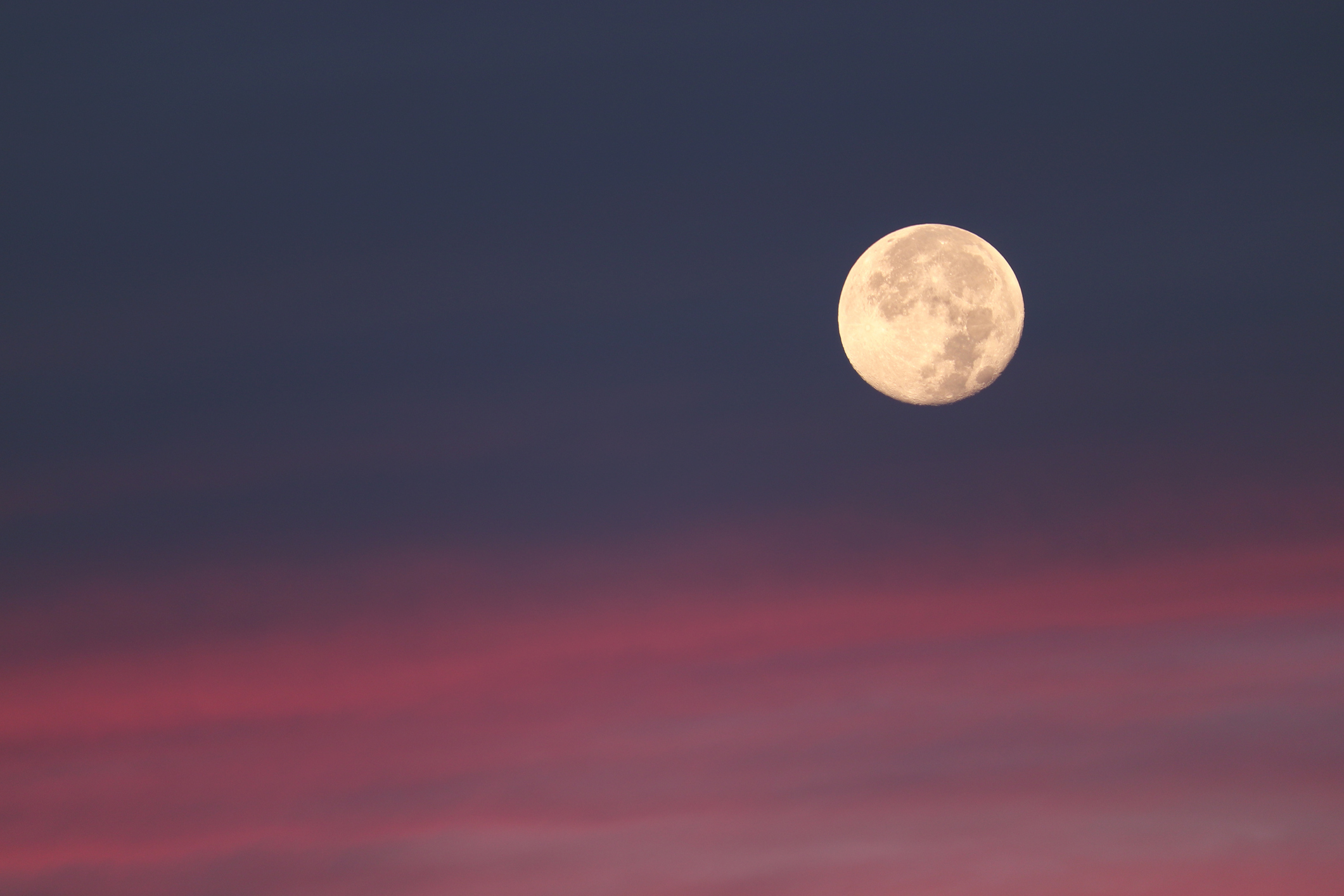 Lua cheia brilhante no céu noturno, com a parte superior azul-escuro e a inferior em tons de rosa e roxo, como um pôr do sol