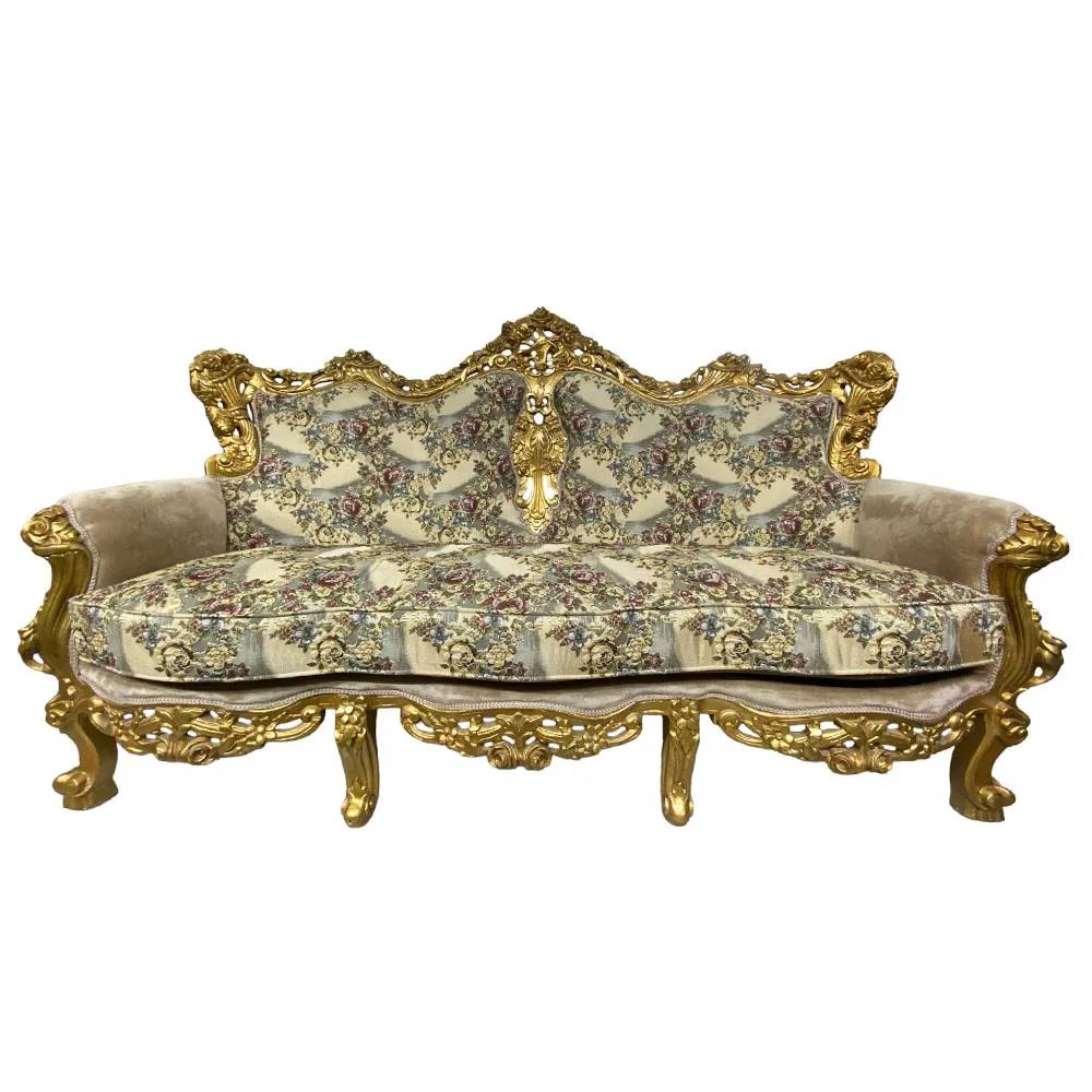 Sof&aacute; estilo Lu&iacute;s XV com estrutura de madeira dourada entalhada, estofamento bege com estampa floral em tons de rosa, verde e azul, e bra&ccedil;os estofados em veludo bege
